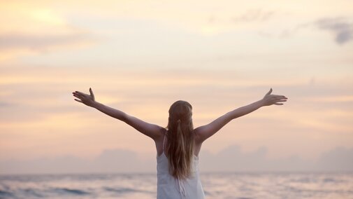 Girl at sunset looking at ocean with open arms.