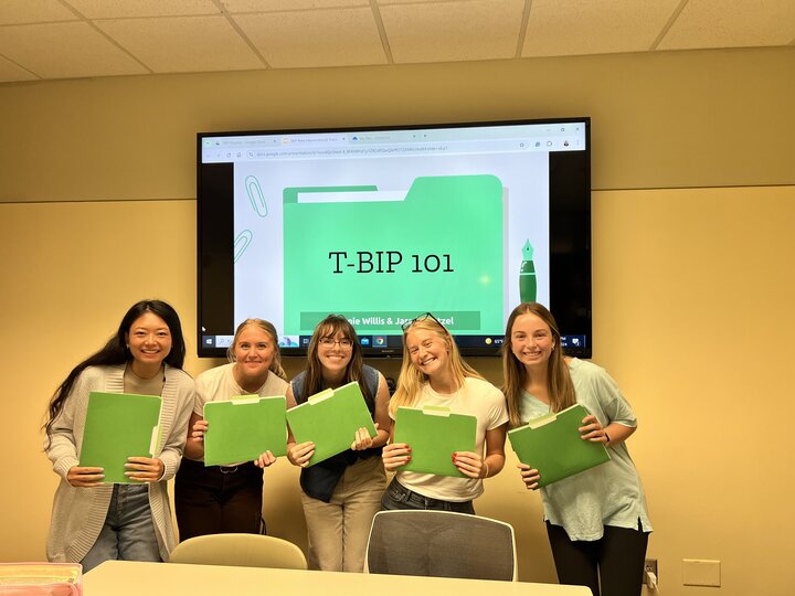 five girls smiling with green folders